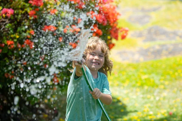 Lindo niño regando flores en el jardín en el día de verano. Niño usando manguera de jardín. Divertido niño regando plantas en el jardín del patio. —  Fotos de Stock