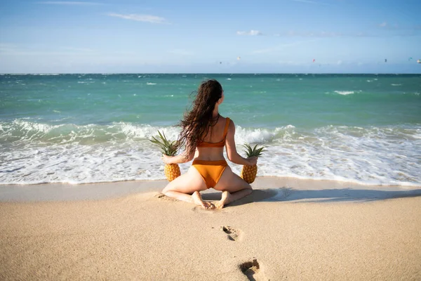 Female buttocks in swimsuit, sexy ass. Woman holding a pineapple on the bali or caribbean beach tropical background with copyspace. — Stok fotoğraf