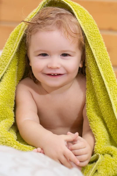 Close up retrato de um pequeno menino loiro cobrir o corpo sob toalha após o banho. Bebê engraçado depois de tomar banho na cama em casa. — Fotografia de Stock