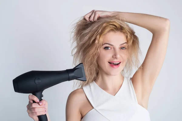 Salud concepto de cabello y belleza. Chica con el pelo rubio usando secador de pelo. Joven atractiva feliz riendo rubia mujer con secador de pelo. Peinado, concepto de peluquería. — Foto de Stock