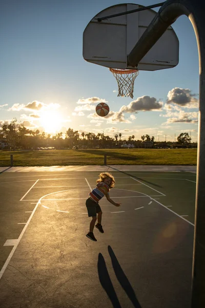 Счастливый маленький мальчик играет в баскетбол на детской площадке. Милый маленький мальчик прыгает с корзинкой мяч для выстрела. — стоковое фото