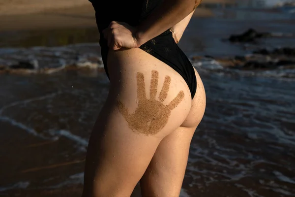 Closeup womans butt with sand hand prints. Perfect womans body. Sexy woman butt with water drops. Sexy beautiful girl in black swimsuit on thailand. Perfect womans body, ass. — Stockfoto