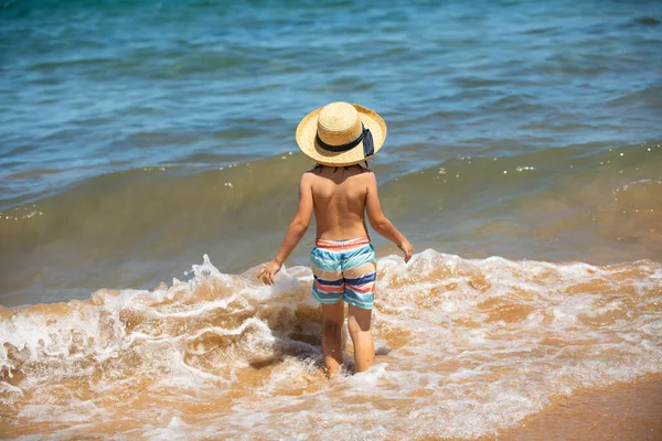海のビーチでの藁帽子の小さな男の子のバックビュー. — ストック写真