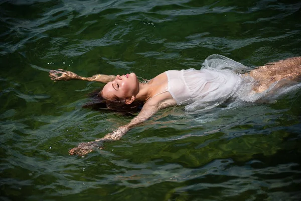 Vacker ung kvinna flyter i hav eller havsvatten, koppla av och ta hand om sig själv. Mode porträtt av graciös söt flicka i sommarklänning under semester på lyx resort. — Stockfoto