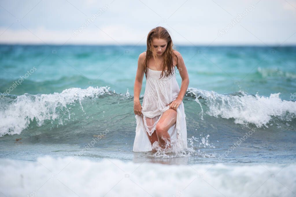 Young sexy woman at waves sea. Summer beach sensual girl. Girl in white dress on tropical beach vacation.