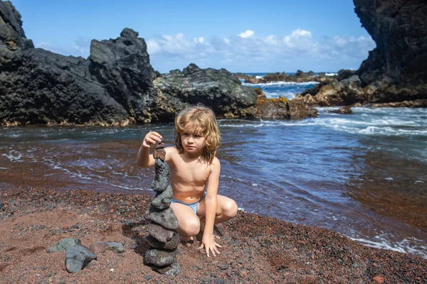 少年は海岸に石の塔を建てることに集中している。夏休みだ。子供は海でリラックス. — ストック写真