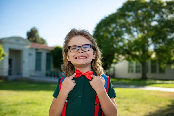 Porträt eines Schülers mit Rucksack in der Nähe der Schule im Freien. Nerd-Schüler bindet Fliege, korrigiert rote Fliege. — Stockfoto