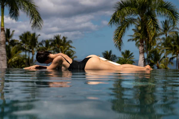 Sexy elegancka kobieta w basenie infinity i cieszy się widokiem na błękitne morze. — Zdjęcie stockowe