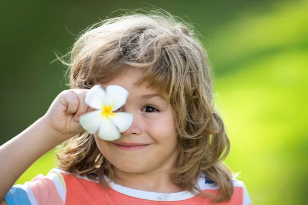 Portrét šťastného smějícího se dítěte s květinou v očích. Uzavřete pozitivní dětskou tvář. Zakrývá oči s květinovou koncepcí. — Stock fotografie