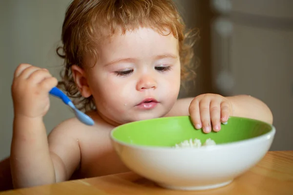 Funny little baby in the kitchen eating with fingers from plate. — Stock Photo, Image