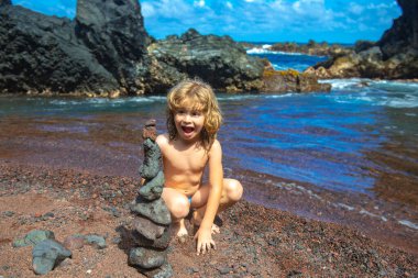 Heyecanlı çocuk çakıl taşı plajında taş piramit yapıyor. Dengeyi, zen, ahengi, dengeyi simgeliyor..