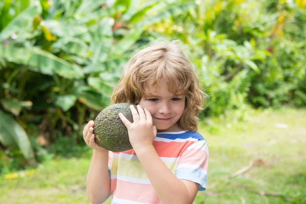 Niño comiendo y disfrutando de un aguacate en un fondo natural. Comida saludable para niños concepto. —  Fotos de Stock