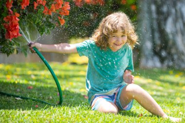Arka bahçede bahçe hortumuyla oynayan komik çocuk. Çocuk su püskürterek eğleniyor. Çocuklar için yaz açık hava aktivitesi.