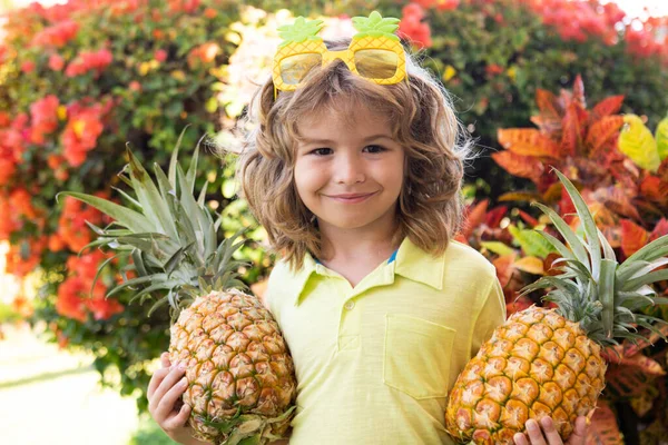 Klein blond kind knuffelt ananas op de achtergrond van de natuur. Jeugd, gezonde voeding, reclame. close-up kinderen grappig gezicht, kopiëren ruimte. — Stockfoto