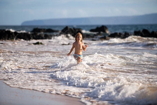Kumsalda koşan küçük çocuk mavi denizde su sıçratıyor. Çocuk yaz plajında yürüyor.. — Stok fotoğraf