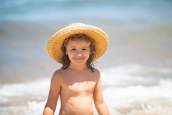 Uroczy chłopczyk w słomkowym kapeluszu na plaży podczas wakacji. Portret zabawnego dzieciaka na tle morza. Zabawna letnia twarz dziecka. — Zdjęcie stockowe