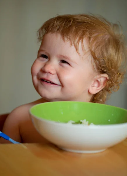 Retrato de criança branca bonito com colher. Bebê bagunçado com fome com prato depois de comer purê. — Fotografia de Stock