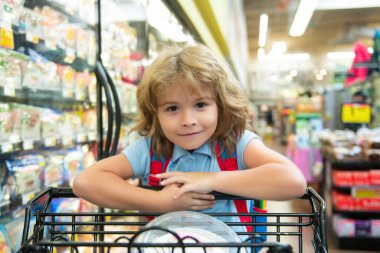 Marketten alışveriş sepeti alan bir çocuk. Müşteri çocuk süpermarketten ürün satın alıyor.