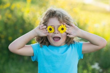 Yazın doğa parkında gözlerinin önünde çiçek tutan heyecanlı çocuğun portresi. Çocuk kavramı yakın planda. Çocuklar yazın tadını çıkarıyor. Gözleri çiçek konseptiyle kaplar.