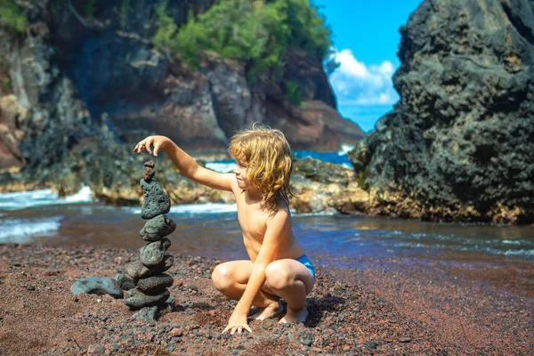 Kid builds a cairn of stones on the sea coast. Beach games with children. Leisure in the evening on vacation with kids. Balance development building fantasy. Childhood. Ocean kids trawel. — Stock Photo, Image