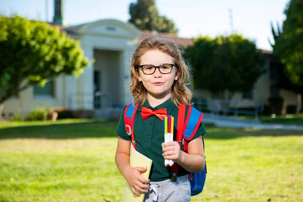 Cleverer Schuljunge mit Brille, Schultasche und Buch in der Hand. Zurück zur Schule. Schülerporträt im Schulpark. — Stockfoto