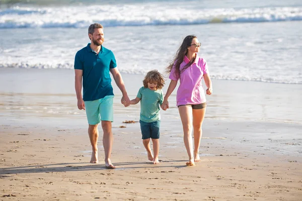 Family walking on beach. Mother father and child son spending time together. Family summer vacation. Parent dad mom walking with son holds hand barefoot on sea.
