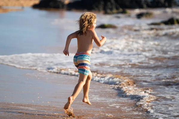Bambino che corre attraverso l'acqua vicino alla riva lungo la spiaggia del mare. Un ragazzo corre lungo la costa del mare. Resto dei bambini in vacanza estiva. — Foto Stock