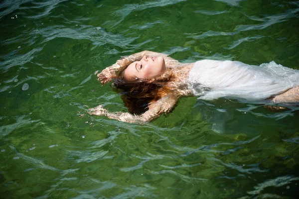 Ung kvinna flyter i hav eller havsvatten, koppla av och ta hand om sig själv. Mode porträtt av graciös söt flicka i sommarklänning under semester på lyx resort. — Stockfoto
