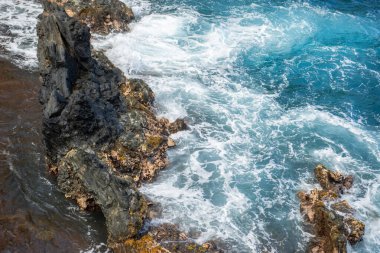 Okyanus dalgaları kayalık ada kıyısına çarpıyor. Okyanus dalgaları ve taşlar sıçrıyor..