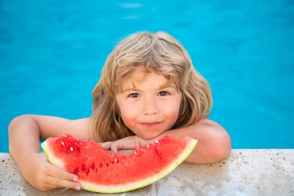 Un niño gracioso juega en la piscina. El niño come una sandía dulce, disfrutar del verano. Niñez despreocupada. — Foto de Stock