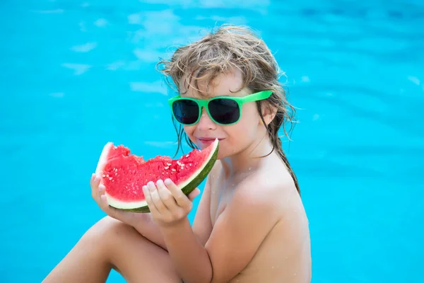 Bambino ragazzo mangiare anguria sulla piscina in occhiali da sole. Faccia divertente per bambini. — Foto Stock