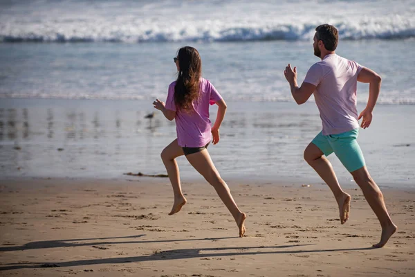 Desportista e desportista a correr juntos à beira-mar. Casal correndo na praia. — Fotografia de Stock