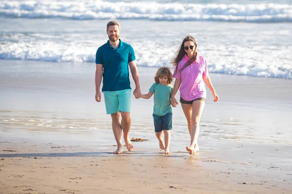 お父さん、お母さん、お子さんが手を取り合ってビーチを歩く. — ストック写真