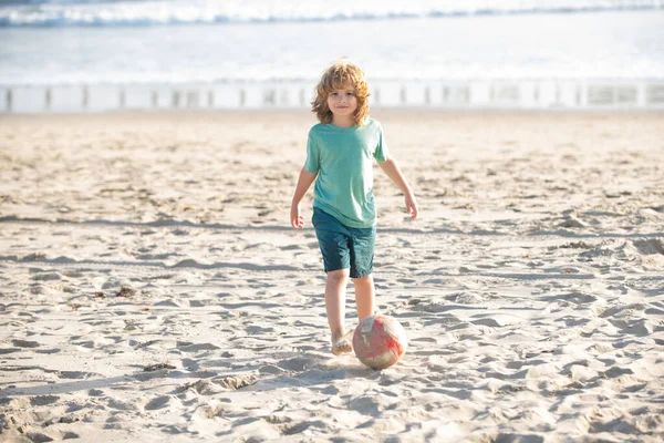 Il ragazzo gioca a calcio sulla spiaggia di sabbia. Calcio estivo sulla spiaggia per bambini. — Foto Stock