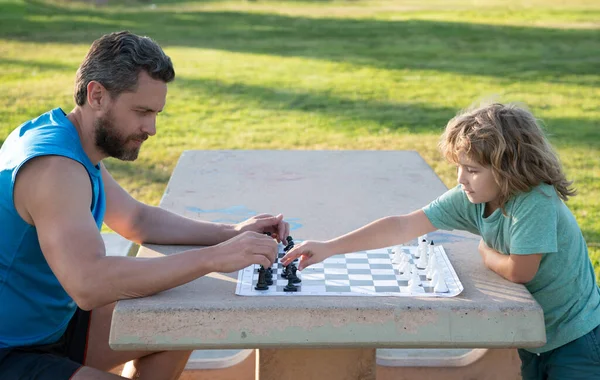 Father and son playing chess spending time together in park. Child playing board game with parent. Men like chess game. Male generation portrait.