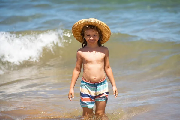 Uroczy chłopczyk w słomkowym kapeluszu na plaży podczas wakacji. Portret zabawnego dzieciaka na tle morza. Zabawna letnia twarz dziecka. — Zdjęcie stockowe