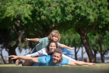 Yaz yürüyüşünde mutlu bir aile. Baba, anne ve çocuk parkta yürüyor. Aileler kırsal kesimde çocuklarına kucak açıyor. Uç konsept, küçük çocuk uçuşu taklit ederken kazma gibidir..