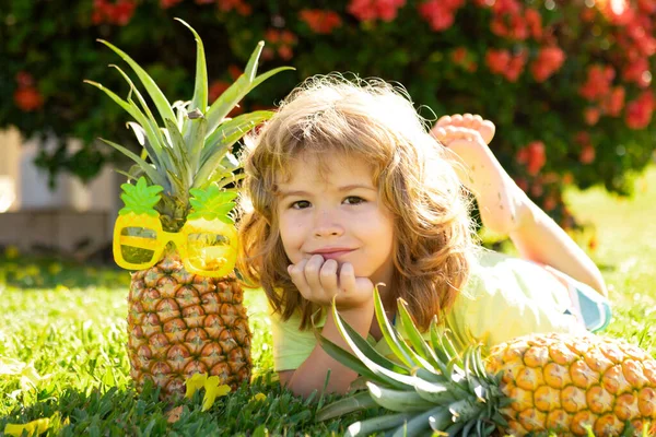 Jovem garoto engraçado segurando abacaxi e sorrindo no quintal. Um miúdo com ananás. Crianças fruta de verão. — Fotografia de Stock