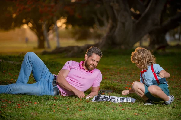 Pai e filho jogando xadrez passar o tempo juntos no parque. Esporte e conceito de hobby. O rapazinho joga xadrez com os pais. Desenvolvimento cognitivo. Jogo de crianças intelectuais. Crianças inteligentes. — Fotografia de Stock