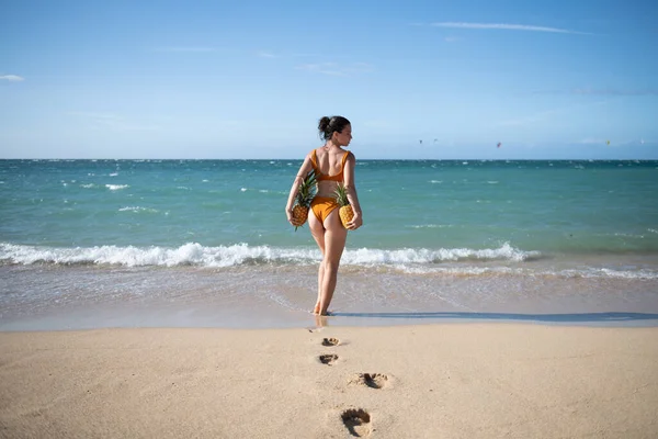 Female buttocks in thongs bikini, sexy ass. Young woman holding a pineapple on sea sand beach background. — Photo