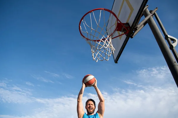 Basketbolcu, tişörtlü ve şortlu sporcu, basketbol topunu şehir arka planında tutuyor. Spor motivasyonu kavramı. — Stok fotoğraf