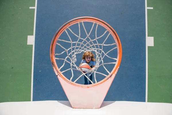 Jogo de basquetebol. Bonito menino segurando uma bola de basquete tentando fazer uma pontuação. — Fotografia de Stock