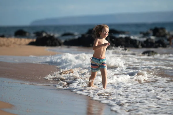 Ragazzo felice che corre sulla spiaggia vicino al mare. Eccitato bambino stupito divertirsi con la corsa attraverso l'acqua in mare o mare. — Foto Stock