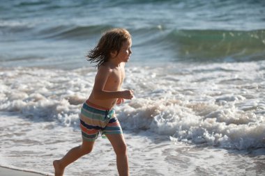 Deniz kıyısına yakın sularda koşan bir çocuk. Bir çocuk deniz kıyısında koşuyor. Çocukların geri kalanı yaz tatilinde..
