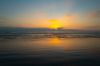 Gün batımında gökyüzü ve bulutların arasında güneş olan sakin bir deniz. Okyanus ve gökyüzü arkaplanı, deniz manzarası.