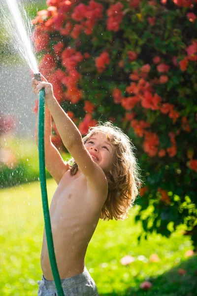 庭の子供の散水花や植物。裏庭にホース付きの子供。子供の園芸。子供夏の楽しい屋外で家. — ストック写真