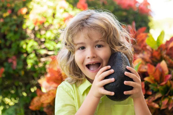 夏の庭でアボカドを見せてくれる幸せな子供。子供の健康食品. — ストック写真
