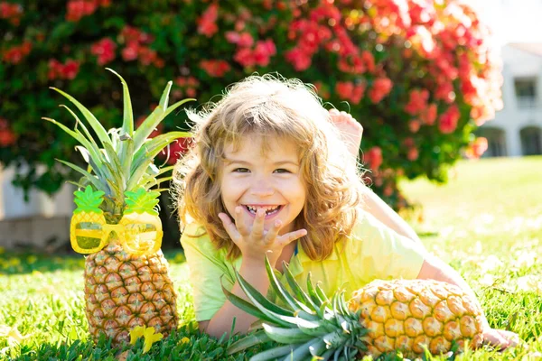 Menino com abacaxi na cabeça, brinca com frutas tropicais frescas ao ar livre. Miúdo engraçado excitado. Rosto de criança com expressão espantada. Crianças festa de verão. — Fotografia de Stock