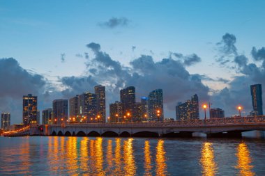 Miami şehri. Alacakaranlıkta deniz üzerinde gökdelenlerle Miami gökyüzü manzarası. Sanset 'te gece.