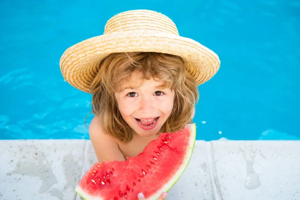 Grabben äter vattenmelon i poolen. Söt pojke äter skiva röd vattenmelon på stranden, glad kaukasisk pojke vattenmelon mot det blå vattnet. — Stockfoto